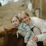 A mother and child enjoy a tender moment with a cow outdoors, embracing nature's warmth.