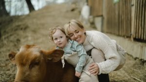 A mother and child enjoy a tender moment with a cow outdoors, embracing nature's warmth.