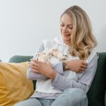 Happy woman sitting on a sofa, smiling and holding pet sugar gliders in a cozy indoor setting.