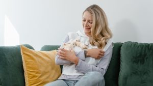 Happy woman sitting on a sofa, smiling and holding pet sugar gliders in a cozy indoor setting.